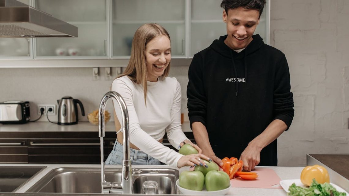 Smiling young couple cooking together in a modern kitchen, slicing fresh vegetables.