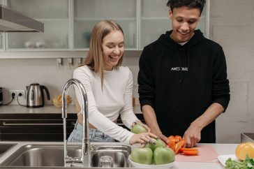 Smiling young couple cooking together in a modern kitchen, slicing fresh vegetables.