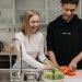 Smiling young couple cooking together in a modern kitchen, slicing fresh vegetables.
